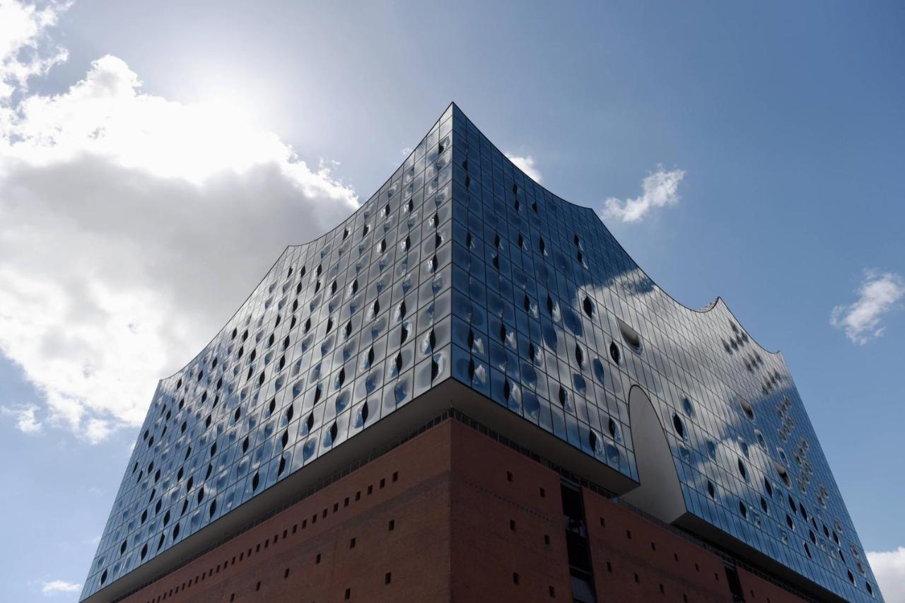 더 웨스틴 함부르크 함브루크 외부 사진 The photo shows a modern architectural building characterized by a distinctive, wavy glass facade. The structure has a bluish tint with many large windows that reflect the sky and surrounding environment. The lower section of the building is made of 