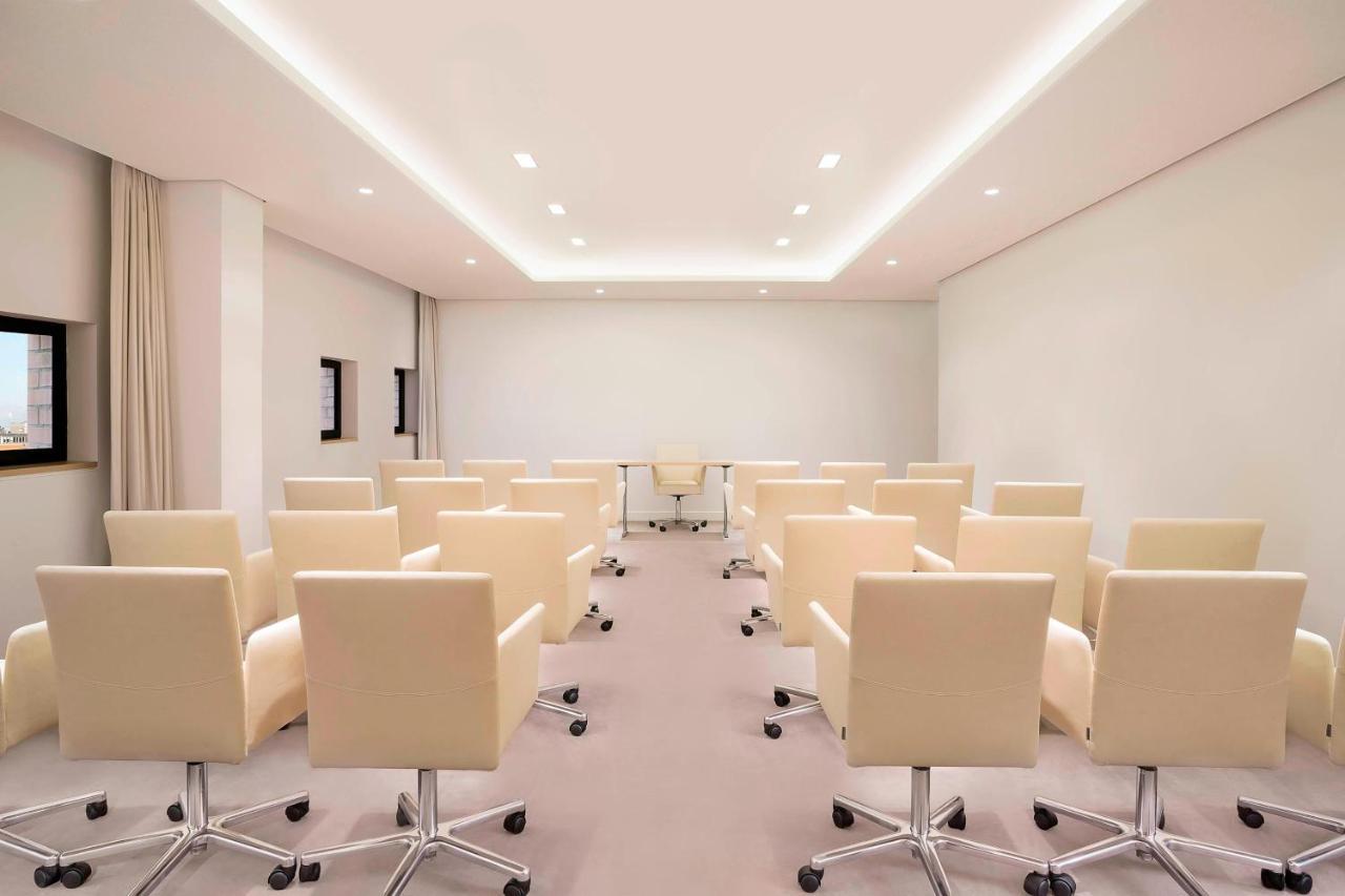 더 웨스틴 함부르크 함브루크 외부 사진 The photo shows a modern conference room. There are several light-colored, wheeled chairs arranged in rows facing a central area where a glass table is located. The room has soft lighting from recessed ceiling lights, and the walls are mostly white, 