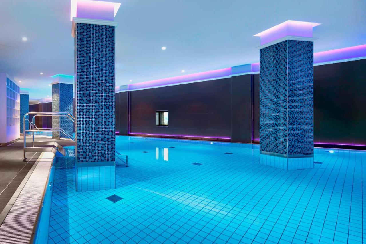 더 웨스틴 함부르크 함브루크 외부 사진 The image shows a swimming pool area that features a modern, upscale design. The pool has bright blue tiles reflecting the water, creating a vibrant atmosphere. There are two columns dressed in a similar blue tile pattern, and the walls are adorned w