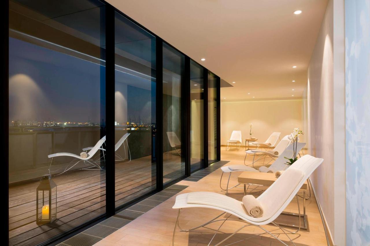 더 웨스틴 함부르크 함브루크 외부 사진 The photo shows a modern, stylish indoor space with large glass windows that offer a view of the night. The area is illuminated softly, highlighting a sleek and minimalist design. There are several white lounge chairs arranged on a wooden deck, creat