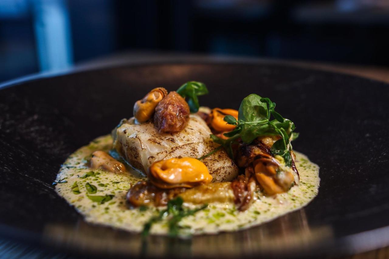 더 웨스틴 함부르크 함브루크 외부 사진 The photo shows a beautifully presented plate of food. It features a piece of fish, likely white fish, which is cooked and garnished with various elements. Surrounding the fish are mussels, possibly in their shells, and some sort of sauce, likely a c